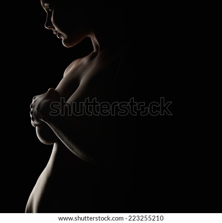 Silhouette of a nude woman covering her breast. Outline of a plus size naked woman against black background.