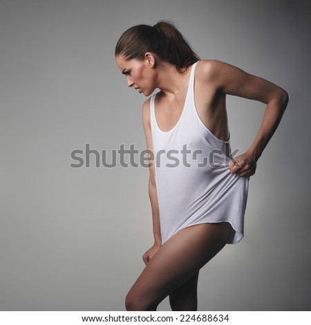 Sexy young woman wearing a tank top posing on grey background. Caucasian female model looking down.
