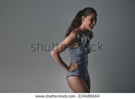 Woman in underwear laughing on grey background. Studio shot of woman wearing bodystocking standing with her hands on hips looking down smiling.