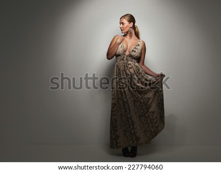Beautiful caucasian woman in an elegant cocktail dress poses in the studio. Oversized female model on grey background.