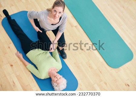High angle view of female trainer helping senior woman do leg stretches at rehab. Gym trainer assisting elder woman in leg stretching workout.
