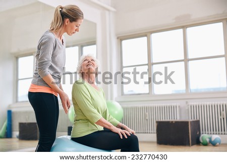 Portrait of a female gym instructor helping an older woman. Portrait of female coach assisting senior woman exercising in health club.