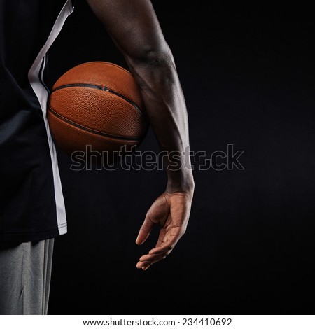 Close-up of a basketball in hand of a young african athlete against black background with copyspace