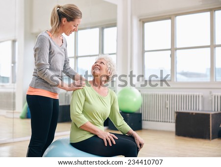 Female instructor assisting senior woman exercising in health club. Older woman assisted by personal trainer at gym.