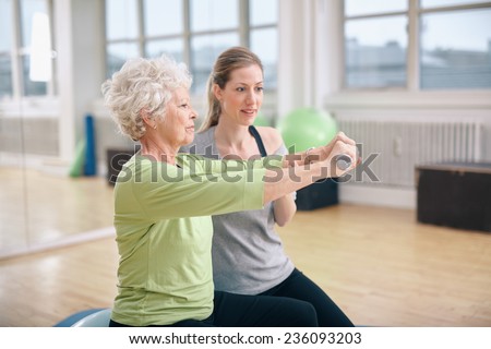 Senior woman being assisted by instructor in lifting dumbbells at gym. Senior woman training in the gym with a personal trainer at rehab.