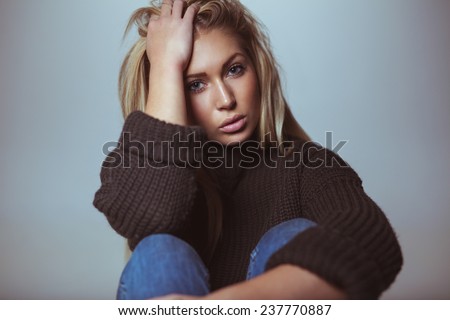 Image of beautiful female model wearing sweater with her hand in hair. Studio shot of attractive woman.