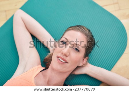 Close-up portrait of gorgeous female smiling while lying on gym floor. attractive fitness woman lying on exercise mat with her hands behind her head looking at camera.