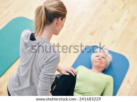 High angle view of female coach helping senior woman exercising in gym.  Gym trainer helping senior woman in leg stretching workout.