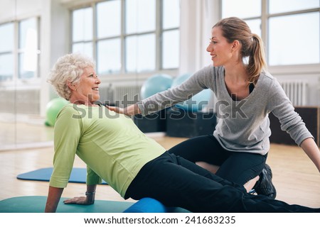 Physical therapist working with a senior woman at rehab. Female trainer helping senior woman doing exercise on foam roller at gym.
