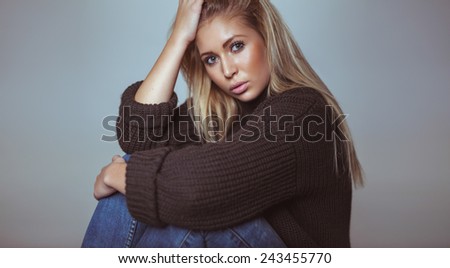 Portrait of beautiful blond female in sweater looking at camera. Pretty young woman in studio.