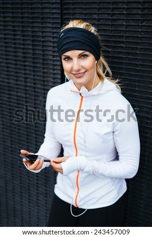 Portrait of attractive young woman listening to music on mobile phone. Female runner relaxing after a training session.