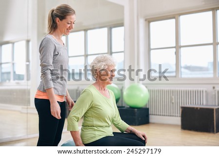 Portrait of female instructor assisting senior woman exercising in gym. Two fitness woman at health club exercising.