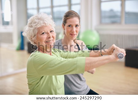 Senior woman exercising with fitness trainer at gym. Active senior woman lifting dumbbells with help from personal trainer.