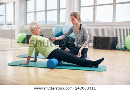 Physical therapist working with active senior woman at rehab.  Old woman exercising using foam roller with personal trainer at gym.