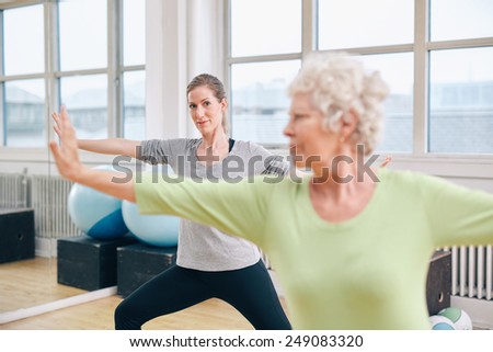 Two women doing stretching and aerobics workout at gym. Female trainer in background with senior woman in front during physical training session