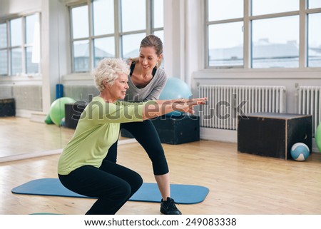 Elderly woman doing exercise with her personal trainer at gym. Gym instructor assisting senior woman in her workout.