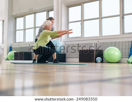 Senior woman doing exercise with her personal trainer at gym. Gym instructor assisting elder woman in her workout.