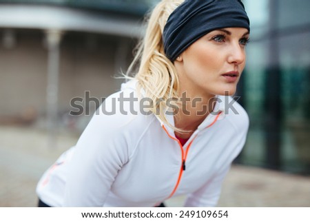 Young woman leaning over in sports gear. Determined sports woman looking forward for run.