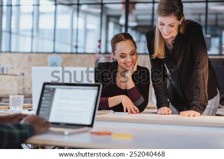 Two young woman at office working on a new creative design. Diverse team of professionals looking at a document smiling.