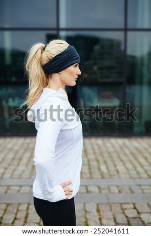 Side view pf young sporty woman standing with her hands on hips outdoors. Caucasian female athlete on street preparing for a city run.