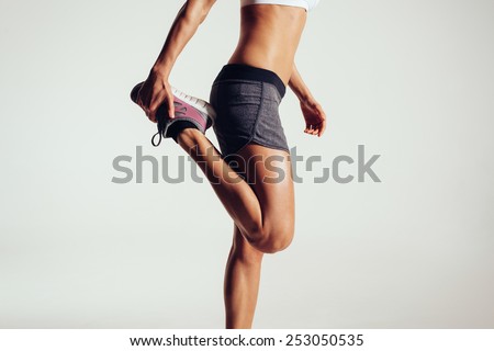 Cropped image of a fitness woman stretching her legs against grey background.  Fit female runner doing stretches.