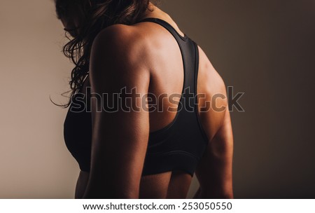 Fit and muscular woman in sports bra standing with her back towards camera. Rear view of fitness female with muscular body.