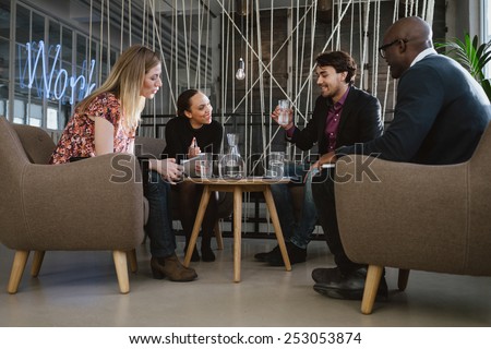 Multiracial business team sitting in office lobby discussing new business ideas. Young man drinking water. Happy young people during meeting.