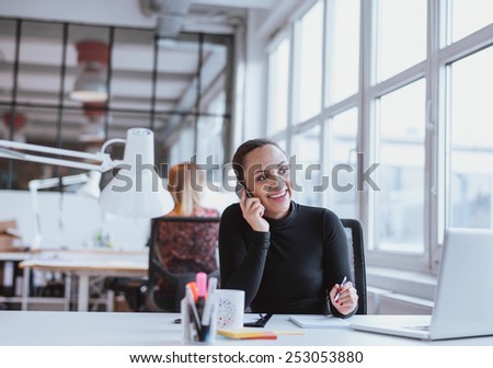 Young african woman using mobile phone while at work. Female executive in conversation on a mobile phone while sitting at her desk.
