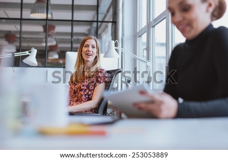 Happy young woman having a friendly chat with her female colleague while at work