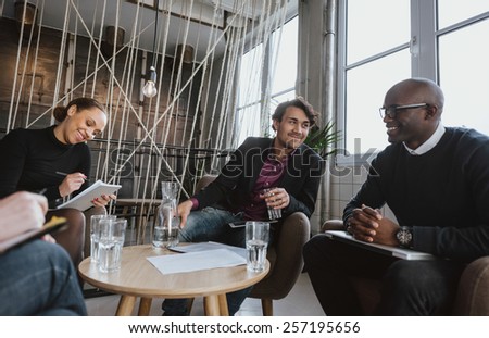 Relaxed young executives having a meeting indoors. Multiracial group of people sitting in office lobby discussing business.