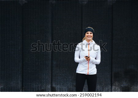 Portrait of happy young woman listening to music on mobile phone. Female runner relaxing after a training session.