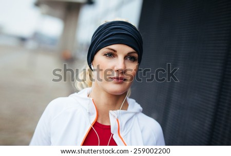 Close-up portrait of attractive and sport woman wearing headband and listening to music on earphones. Fitness female looking relaxed outdoors