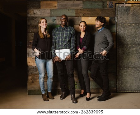 Portrait of young professionals laughing while standing together in office. Multi ethnic business team looking happy together.