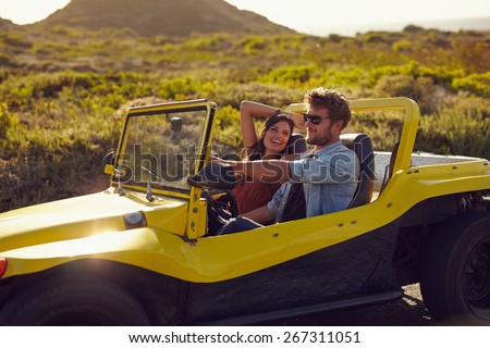 Portrait of happy young couple on a road trip in a beach buggy. Smiling young woman with her boyfriend driving car in countryside.