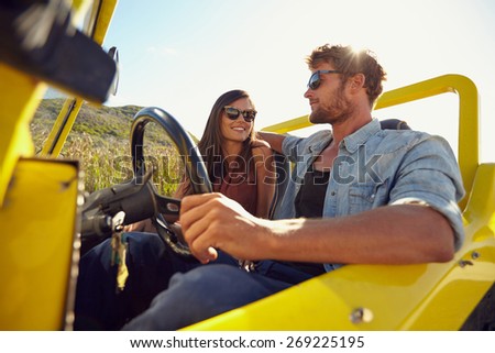 Happy young couple in their car going on a road trip. Young man driving car with woman sitting by on a summer day.