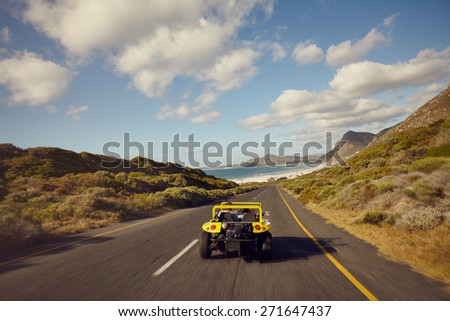 Rear view of couple driving in small car on open road. Young man and young woman on road trip on a beautiful summer\'s day.