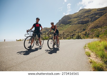 Two young athletes taking a break from cycling on country road. Cyclist training for triathlon competition on open road with bicycles.
