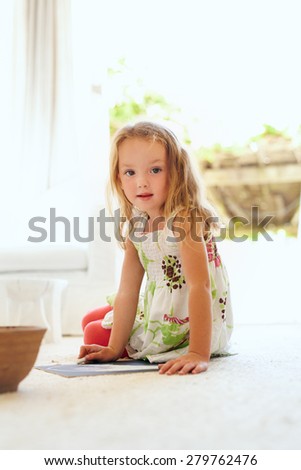 Portrait of cute little girl drawing while sitting on floor at home looking at camera. Elementary age young girl sitting in living room drawing.