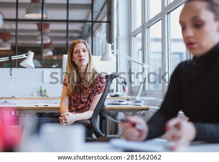 Image of young woman sitting at her desk looking away thinking. Female executive in office lost in thought.