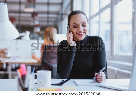 Happy young woman sitting at her desk working and answering a phone call.