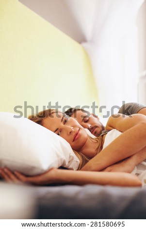 Young couple lying together on bed. Beautiful young woman lying on bed and looking at camera with her husband sleeping.