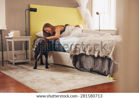 Woman lying on bed playing with her pet dog in morning. Man sleeping in background.