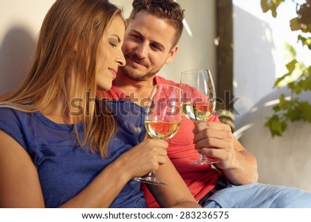 Young couple celebrating with white wine together, outdoors. Young man and woman toasting wine glass while sitting close together in backyard.