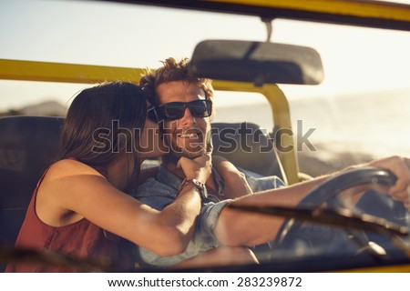 Loving young couple on road trip. Woman kissing her boyfriend\'s cheeks. Young man driving a car. Romantic young couple enjoying the drive on summer day.