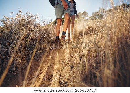 Low angle view of young couple walking on country trail path. Couple hiking on mountain coming downhill. Cropped shot focus on legs.