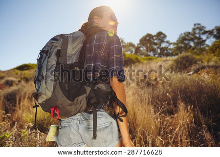 Rear view shot of young woman hiking on summer day. Caucasian female hiker on mountain looking away at a view with sun flare.