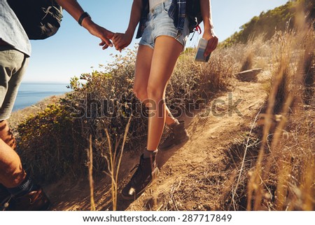 Close-up shot of young couple on a hiking trip. Cropped image of young man and woman hikers holding hands while walking on mountain trail.