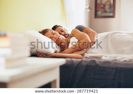 Young adult couple sleeping peacefully on the bed in bedroom. Young man embracing woman while lying asleep in bed.