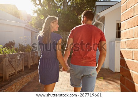 Rear view shot of a young couple taking a walk holding hand in hand outside in their backyard. Loving young couple outdoors on a bright sunny day.
