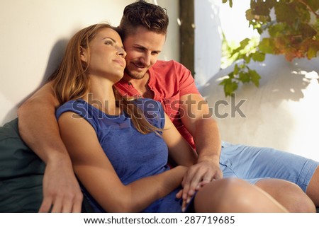 Outdoor shot of romantic young couple sitting together on couch in backyard. Young man and woman in love spending time together.